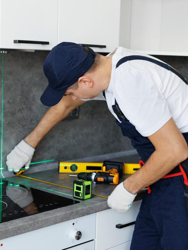 Man in uniform measures the level of the countertop with ruler and laser when assembling furniture
