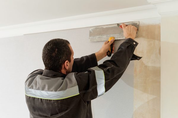 Man is cutting wallpaper. Maintenance repair works renovation in the flat. Apartment renovation and restoration idea indoors.