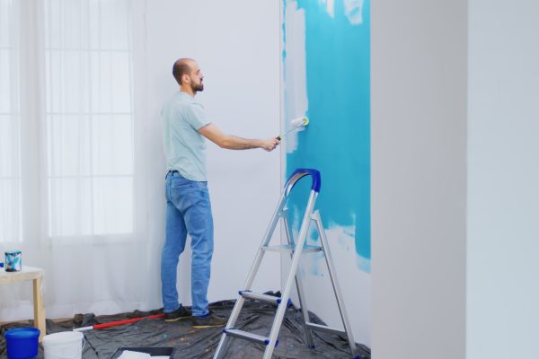 Painting apartment wall with white paint using roller brush. Handyman renovating. Apartment redecoration and home construction while renovating and improving. Repair and decorating.
